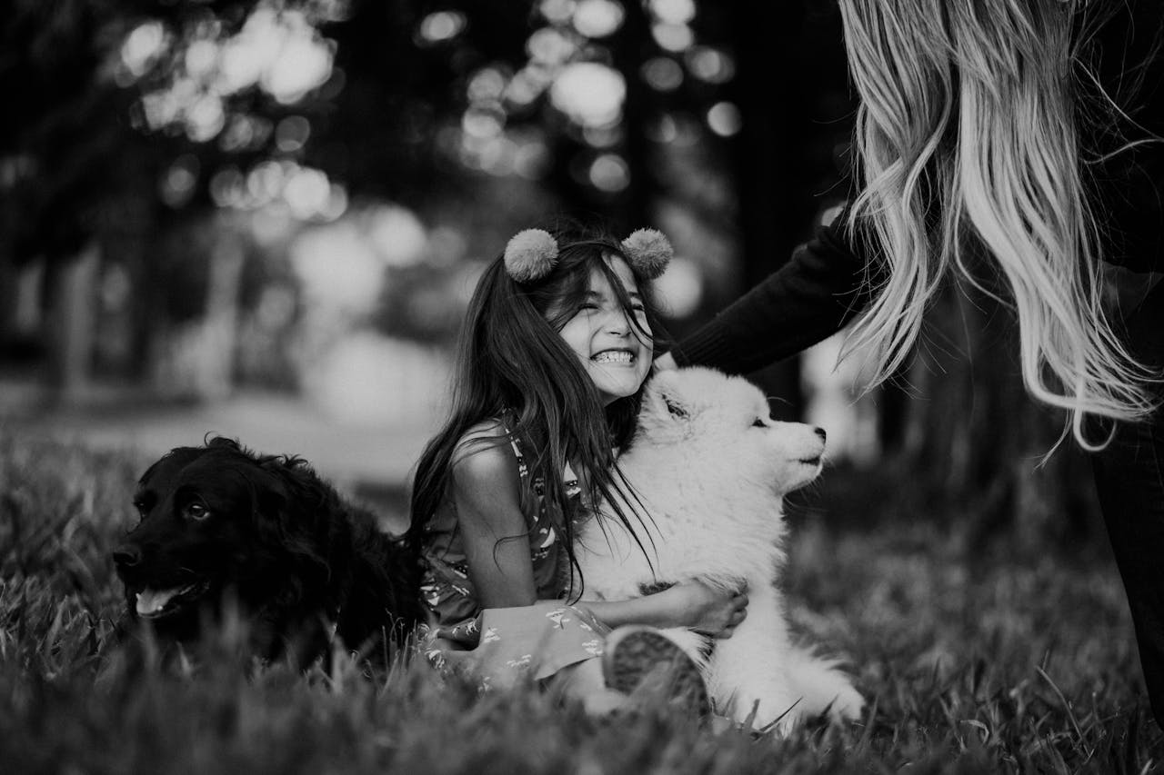 Black and white crop unrecognizable mother touching glad daughter hugging cute puppy during weekend in park